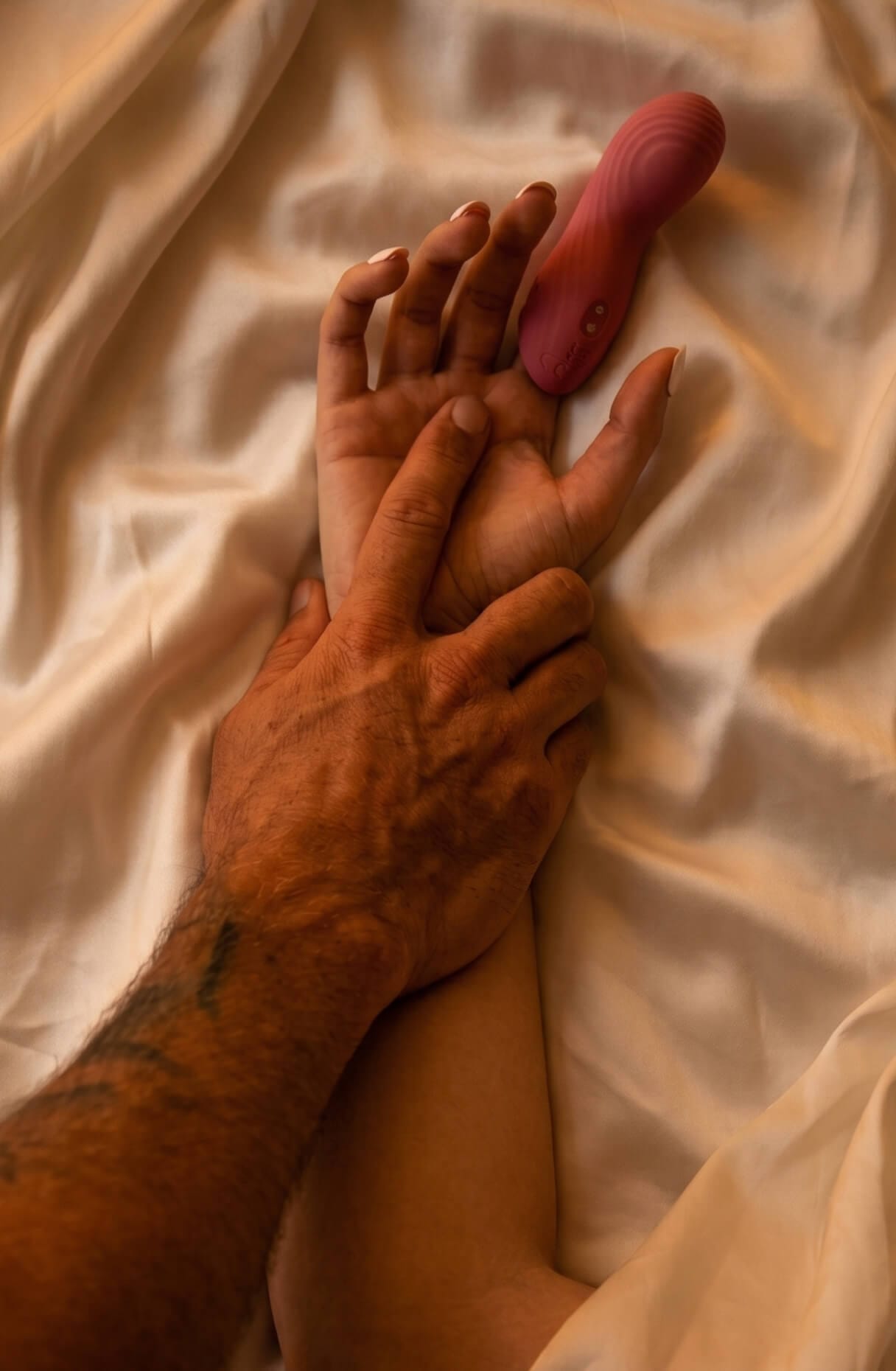 Hands and a vibrator on silk sheets